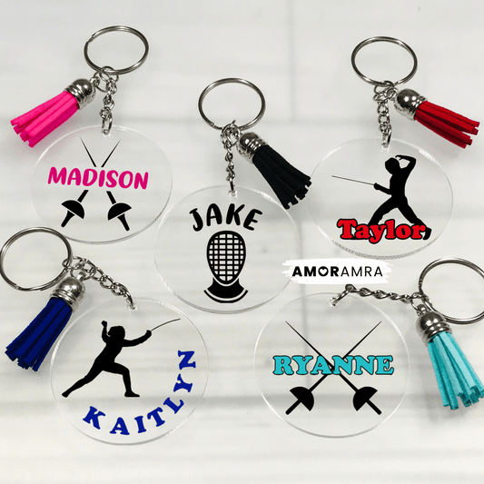 Set of personalized keychains with names and fencing symbols on a white background. Five clear acrylic keychains with different designs and names. The keychains are round and have a silver key ring and a tassel. The designs include a fencing mask, crossed swords, and a silhouette of a fencer. Personalized Fencing Keychain, Fencing Tag, Fencing Gift, Fencing Coach Gift, Girls Fencing, Fencing Sword, Fencing Mask, Fencing Team Gift