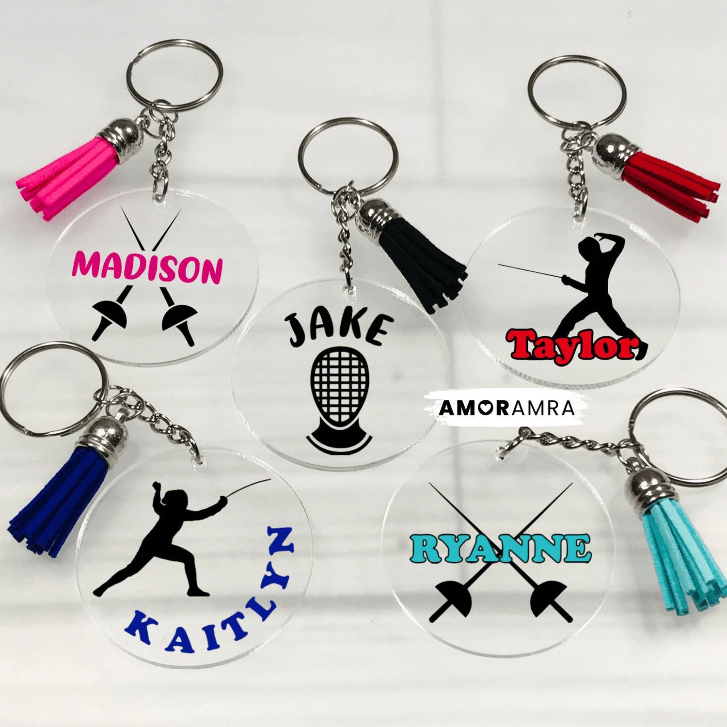 Set of personalized keychains with names and fencing symbols on a white background. Five clear acrylic keychains with different designs and names. The keychains are round and have a silver key ring and a tassel. The designs include a fencing mask, crossed swords, and a silhouette of a fencer. Personalized Fencing Keychain, Fencing Tag, Fencing Gift, Fencing Coach Gift, Girls Fencing, Fencing Sword, Fencing Mask, Fencing Team Gift