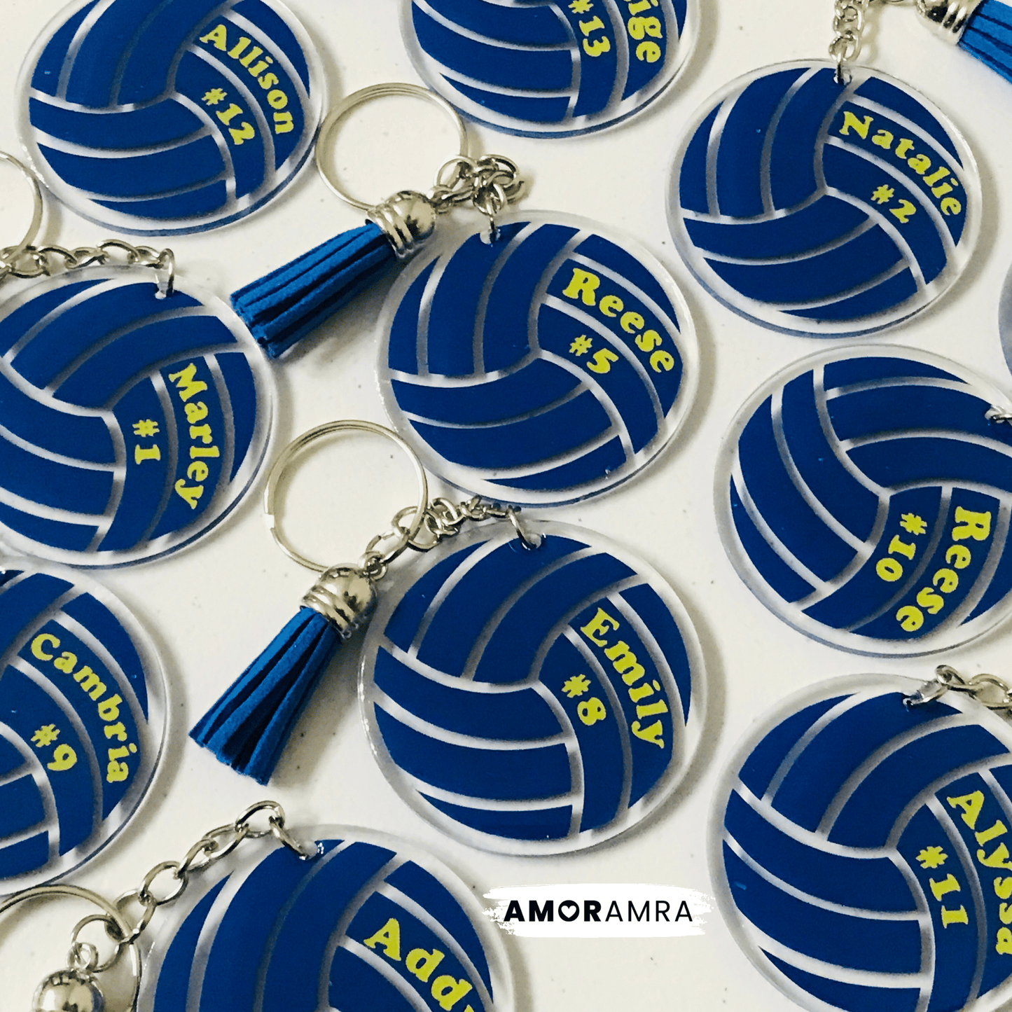 Blue volleyball-shaped keychains with names and numbers on a white background, branded 'AMORAMA'.