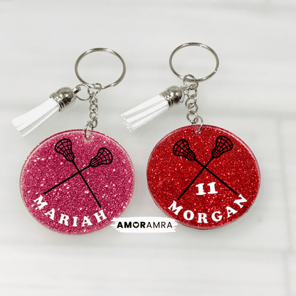 Two red glittery keychains with lacrosse designs and names on a white background