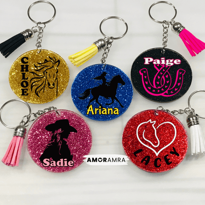 Personalized Glitter Horse Keychain. glitter horseshoe keychain. horse rider keychain. glitter round keychains with different horse themed designs and names. The gold keychain has a horse silhouette. The blue keychain has a silhouette of a person riding a horse. The black keychain has a horseshoe design. The pink keychain has a silhouette of a person wearing a cowboy hat. The red keychain has a heart with a horse silhouette inside. Personalized Horse Keychain, Horse Lover, Equestrian Keychain, Horse loss 